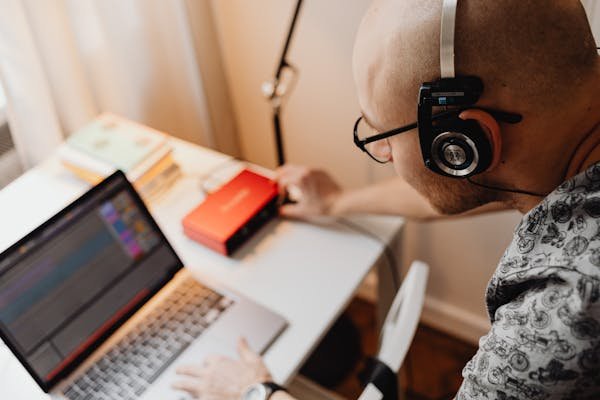 A bald man with headphones working on audio equipment in a modern workspace.