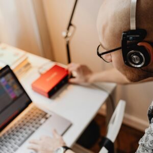 A bald man with headphones working on audio equipment in a modern workspace.