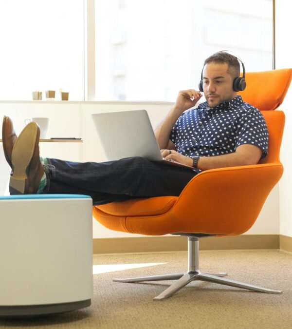 A man relaxes while working remotely in a modern office with a laptop and headphones.