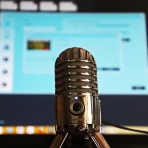 Close-up of a microphone with a blurred computer screen in the background, ideal for podcast themes.