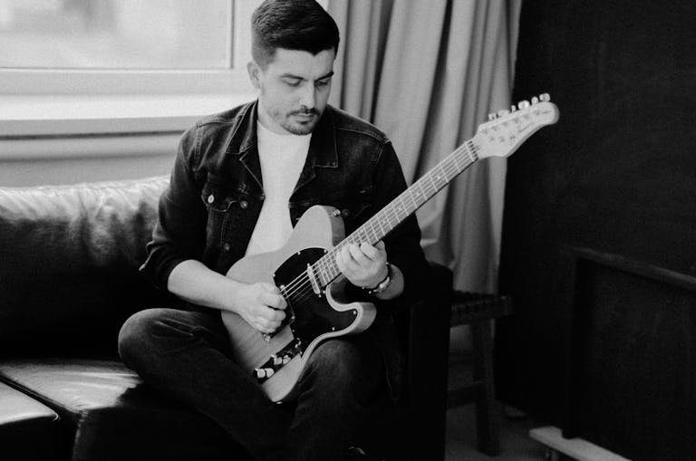 Grayscale Photo of Bearded Man Playing Electric Guitar