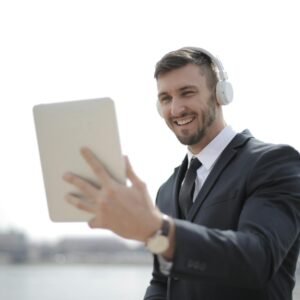 Professional man in a suit smiling while using a tablet with headphones outdoors.